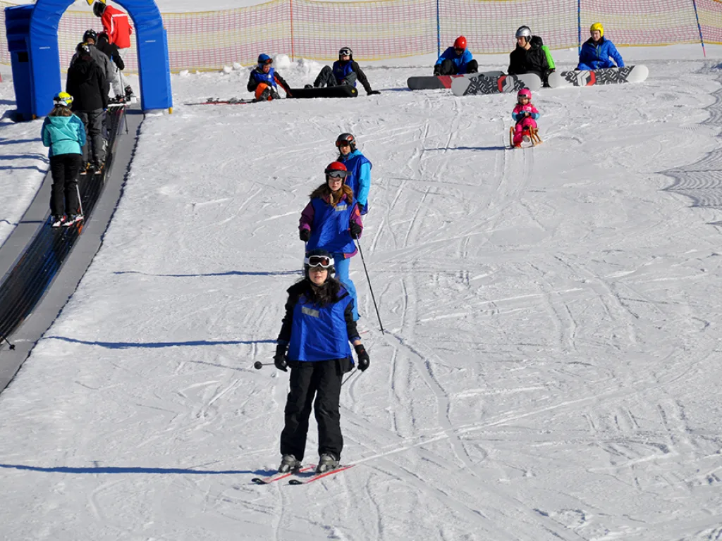 Skifahrerin fährt neben dem Förderband des Übungslifts talwärts.